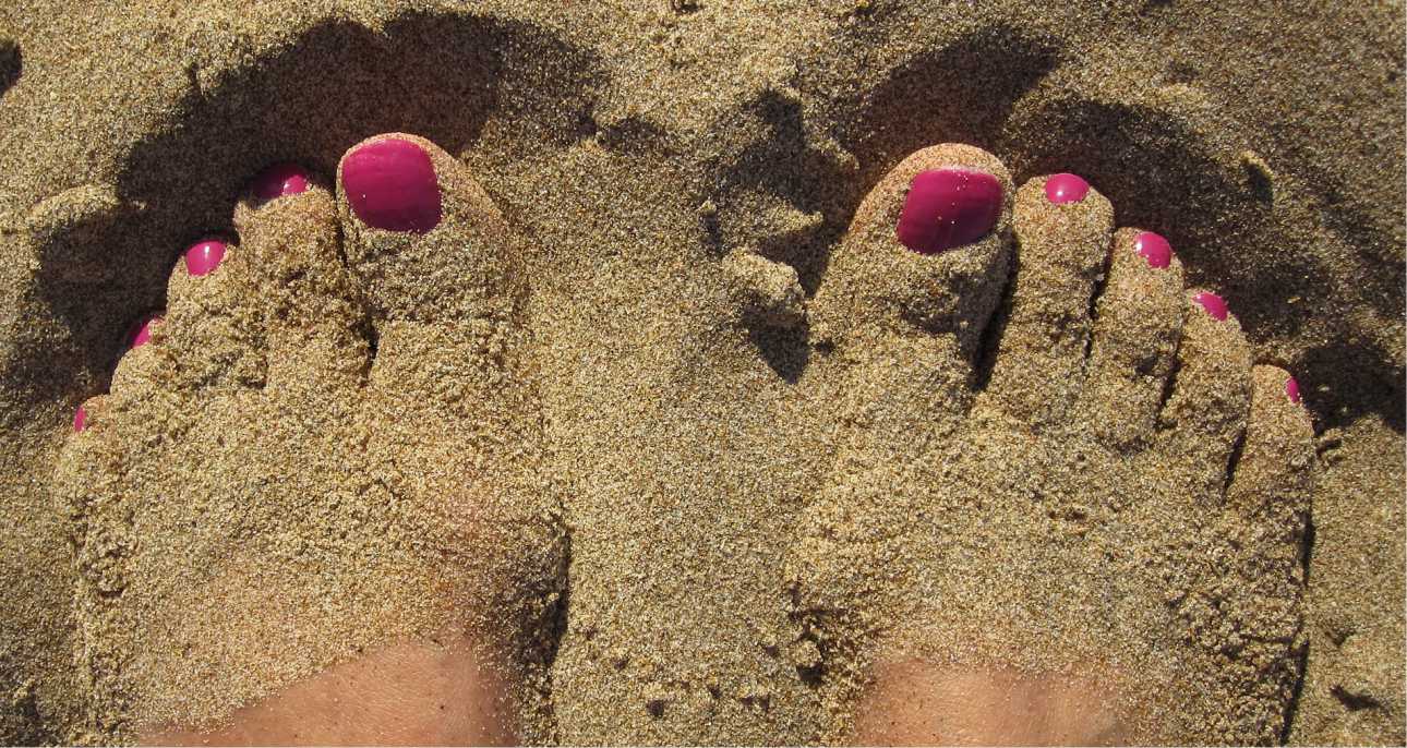 Slika prikazuje stopala v pesku od plaže, slika se uporablja za članek naravna nega stopal.