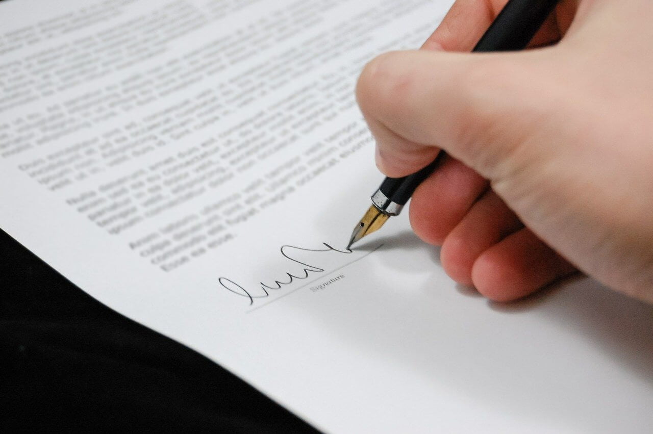 Na sliki je prikazan da se nekdo podpisuje pod pogodbo za pogoji poslovanja.