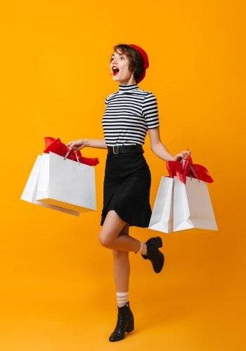Slika prikazuje mlado dekle, ki je zelo navdušena in vesela nad akcijami in popusti. v rokah drži 4 nakupovalne vreče.